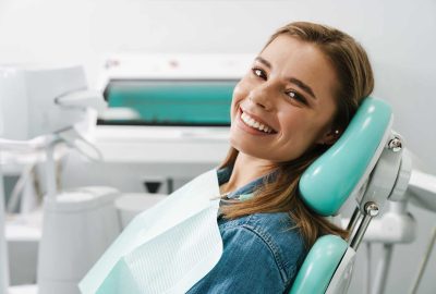 European young woman smiling while sitting in medical chair at dental clinic